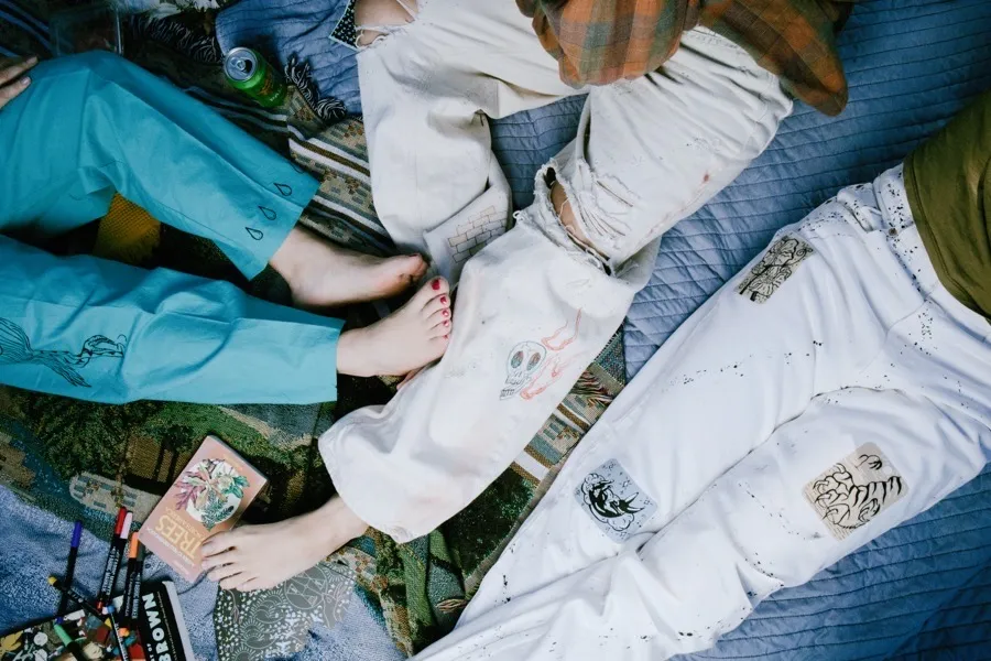 Feet and legs on a blanket showing multiple pairs of hand-painted white pants with skull and nature motifs