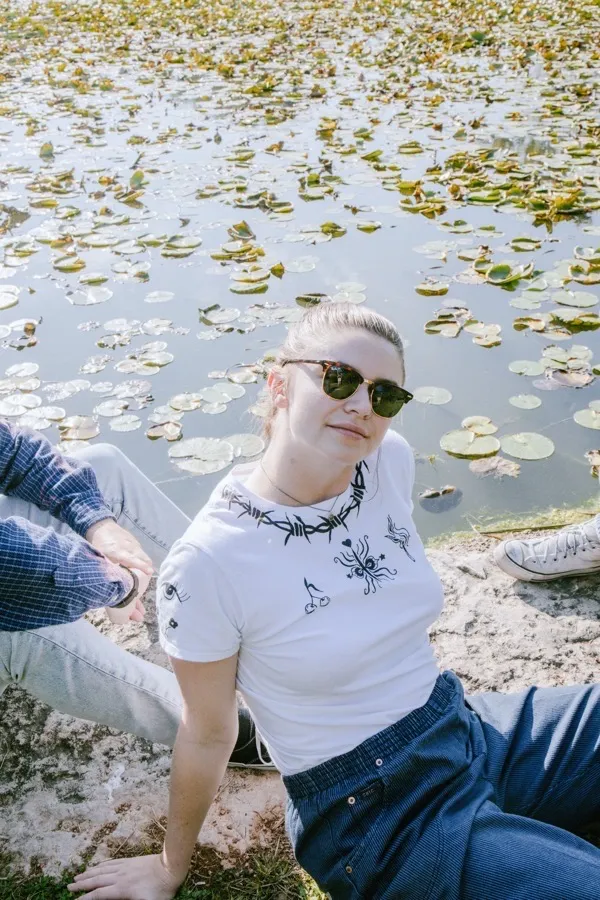 Taylor sitting by a lily pond wearing a hand-painted barbed wire tee