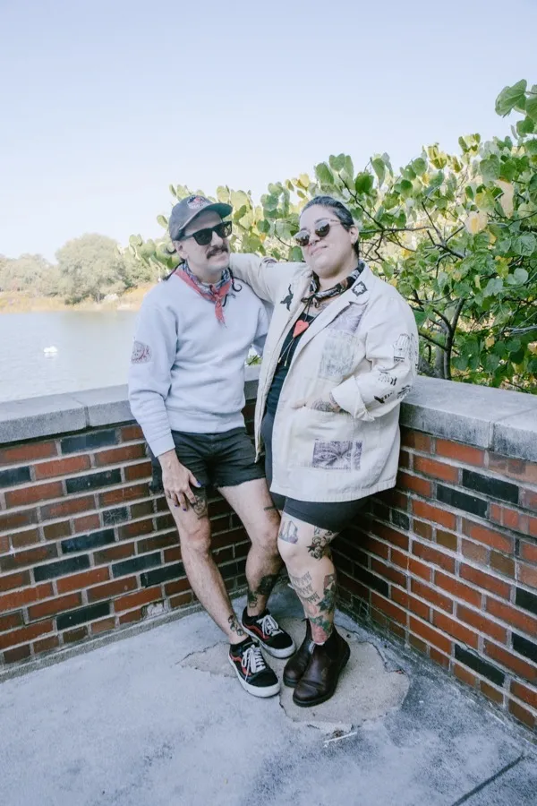 Two people leaning against a brick overlook by the water, wearing Found Slowly pieces